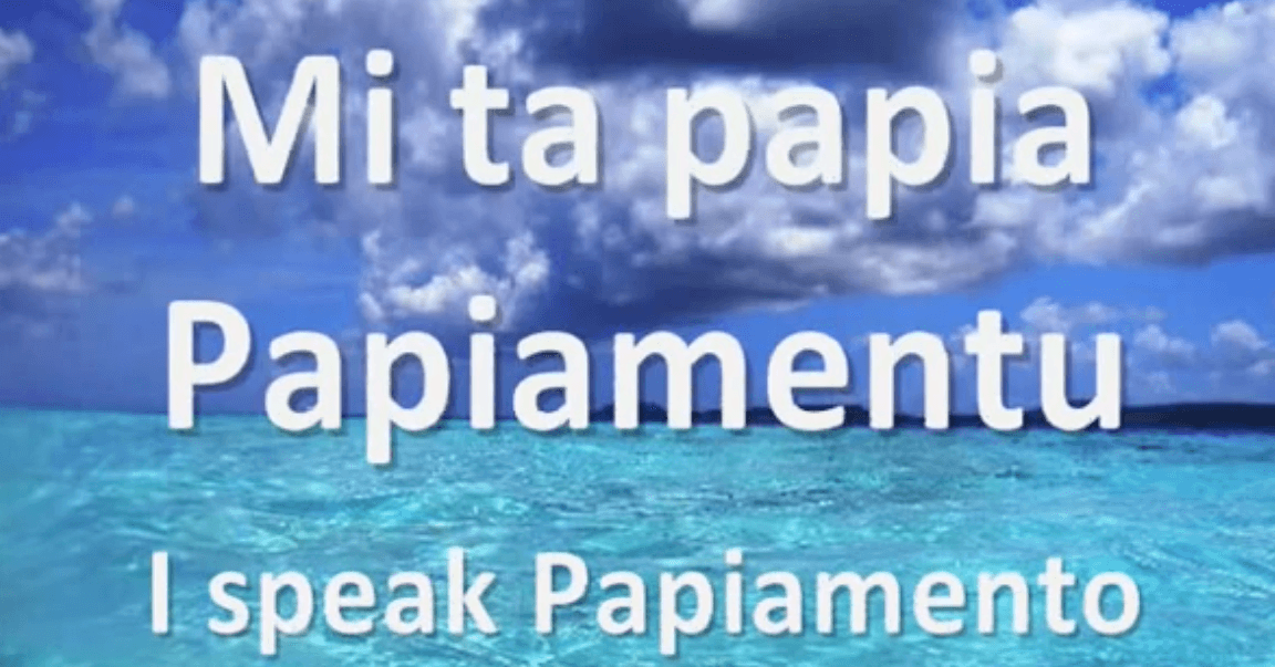 Text reads Mi ta papia Papiamentu. I speak Papiamento over a bright blue ocean near Curacao, under a partly cloudy sky with sunlight reflecting off the water. The scene looks tropical and inviting.