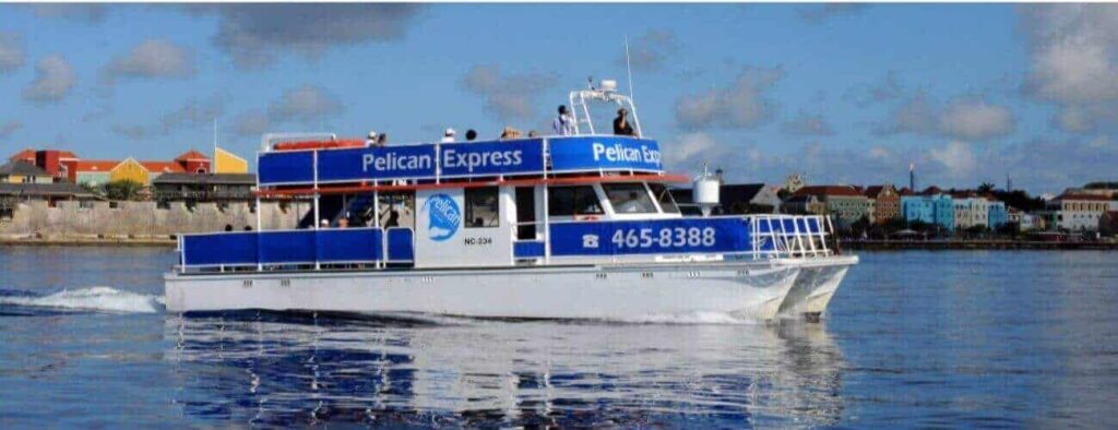 A white and blue ferry, Pelican Express, offers the Guided Snorkel Tour on calm waters. The ferry displays 465-8388, with several people onboard and colorful waterfront buildings under a cloudy sky in the background.