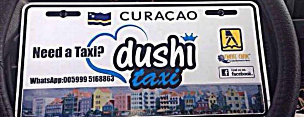 Taxi to Boca Tabla sign: “Need a Taxi? dushi taxi” with WhatsApp number, Facebook icon, colorful buildings below, Curacao flag and blue sky above. Includes business logos and info for Taxi to Boca Tabla service.