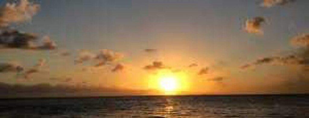 Bubbles on the boat" captures a yellow-orange sunset over calm ocean waters, where warm reflections dance as a small boat drifts near rising bubbles and golden-tinted clouds float in the softly illuminated sky.