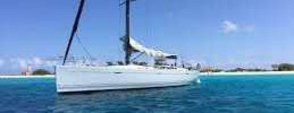 Een witte zeilboot dobbert op helderblauw water bij een zandstrand met groen onder een heldere hemel - perfect voor een Halve dagtocht watersport.