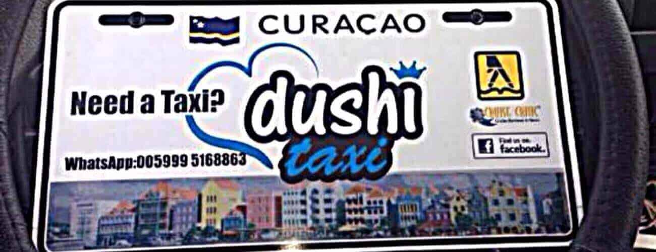 A taxi sign for "Taxi to Playa Porto Marie" features “Need a Taxi? dushi taxi” with a blue heart, phone number, Facebook icon, colorful waterfront buildings, three logos including the Curacao flag, and offers rides to Playa Porto Marie.