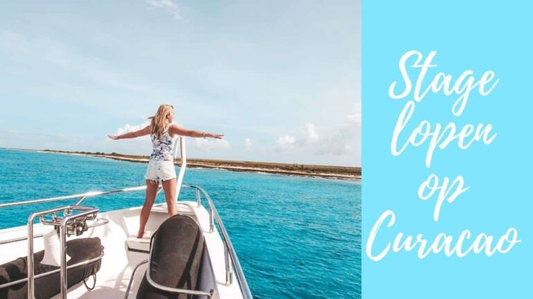 A woman stands at the bow of a boat with arms outstretched, facing Curacao’s clear blue water and a distant shoreline under a partly cloudy sky. On the right, a light blue box displays white cursive text: Stage lopen op Curaçao.