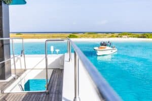 Geniet van het idyllische uitzicht op turquoise water, een zandstrand en weelderig groen vanaf het dek van je jacht met Klein Curacao All-In Reis - een complete reiservaring bij Klein Curacao onder een strakblauwe hemel.